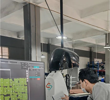 An operator seated at a cutting station, a monitor beside the machine showing the cut layout on screen